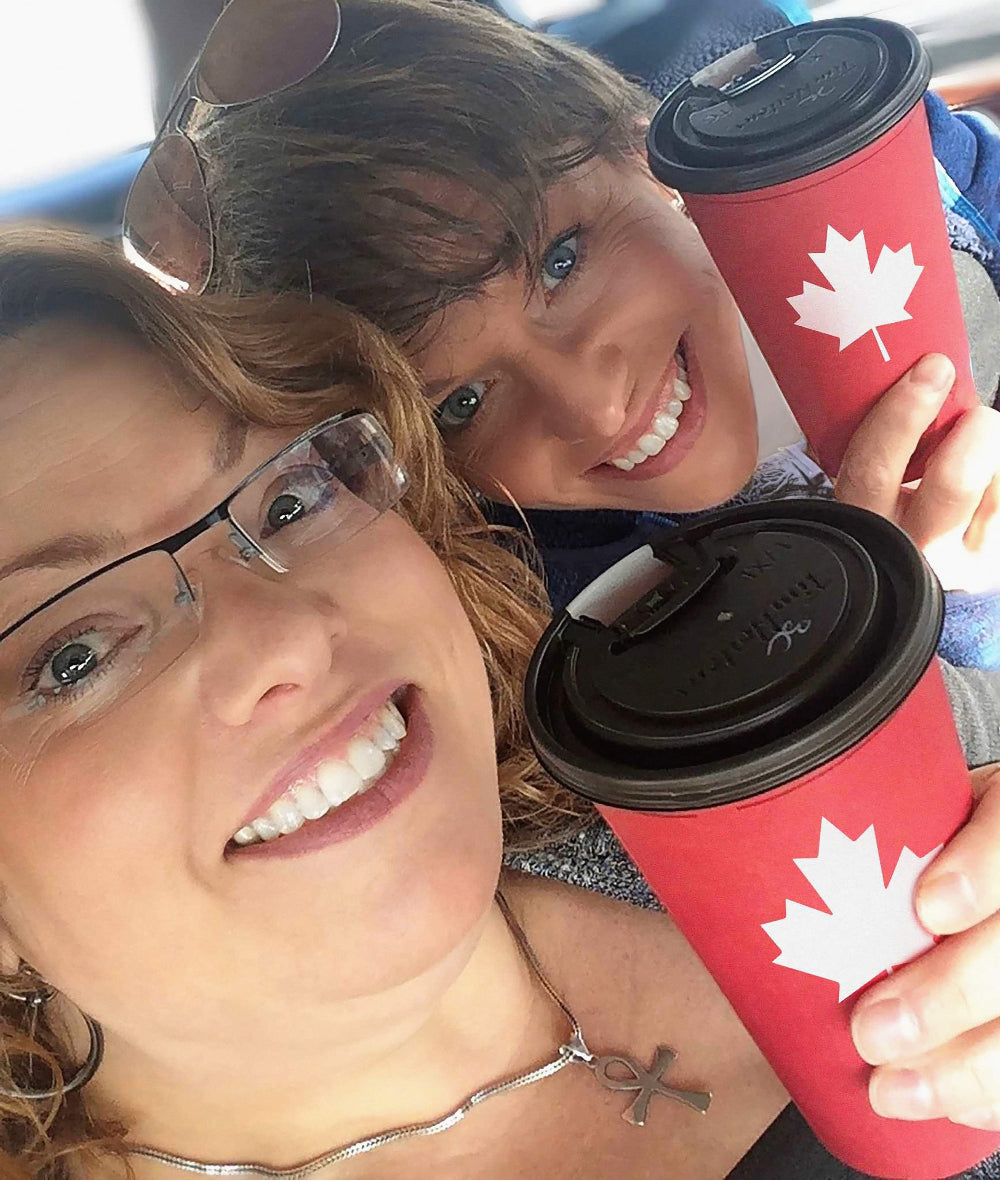 Two sisters holding Tim Hortons coffee cups with Canadian maple leaf designs.