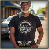 A confident older man stands proudly in the middle of a sunny small-town street, wearing the Tone Out retro-style black t-shirt. The shirt features a bold vintage microphone and laurel design with a distressed red and white color scheme. Below the main design, the SR Wear-A-Tude logo is prominently displayed. He pairs the shirt casually with jeans and a ball cap, giving off a relaxed, street-smart vibe perfect for everyday wear.

